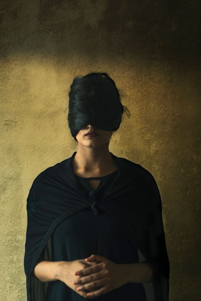 A conceptual portrait of a woman in a dark dress with eyes covered by her hair.