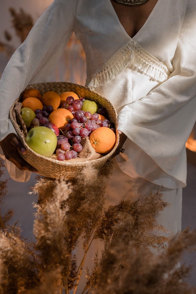 A stylish woman in white holding a basket of fresh assorted fruits outdoors.