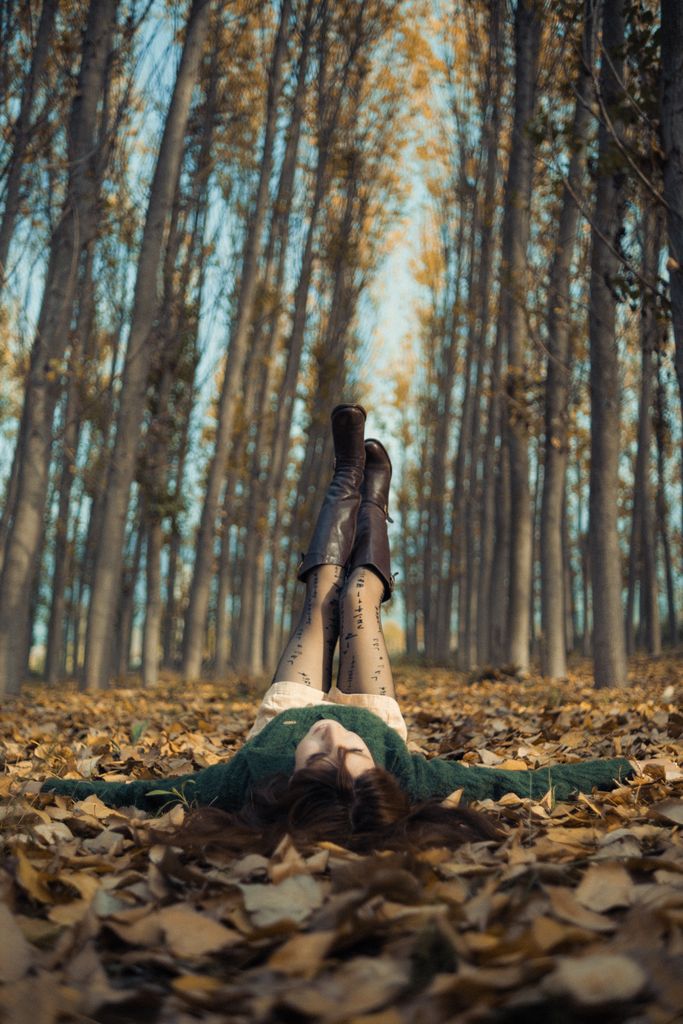 A woman lying on fallen leaves in a forest, enjoying a peaceful autumn day.