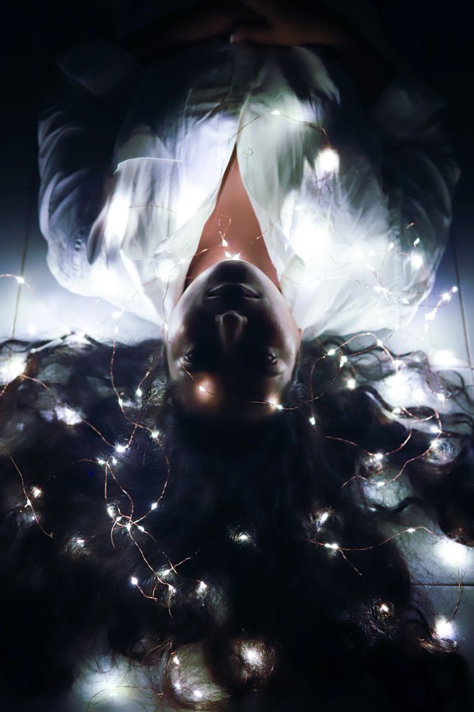 Top view of a woman lying with glowing fairy lights, creating an artistic and dreamy effect.