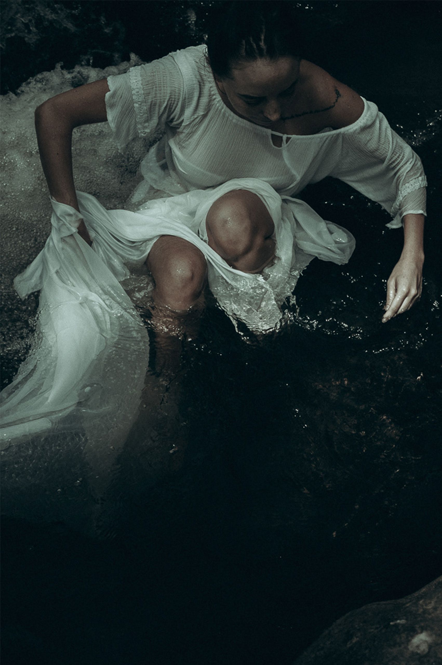 A woman in a white dress sits in a river at night, creating a mysterious and serene atmosphere.